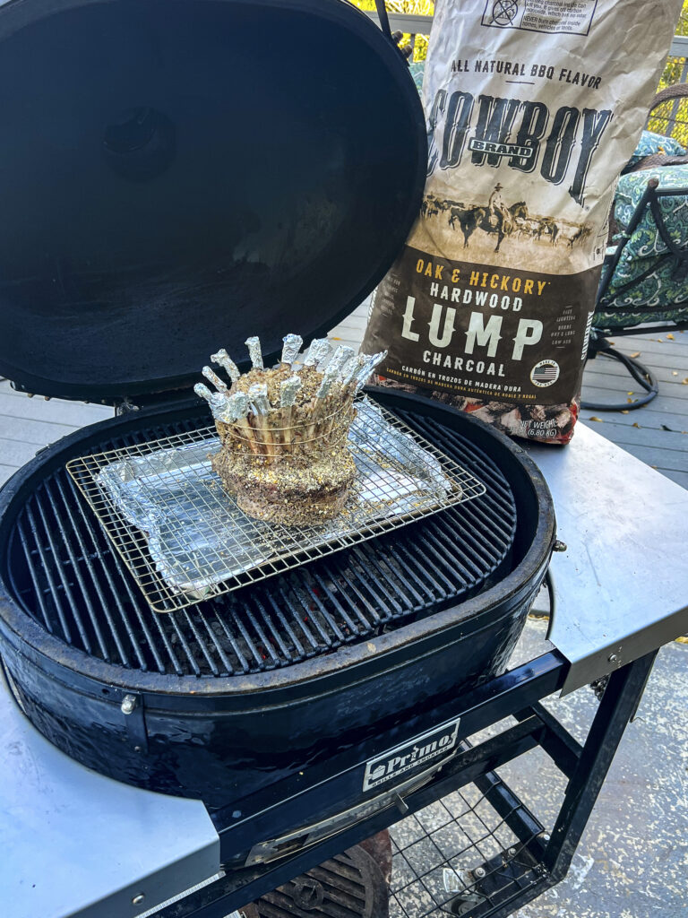 A crown of lamb is on the grill grates. 