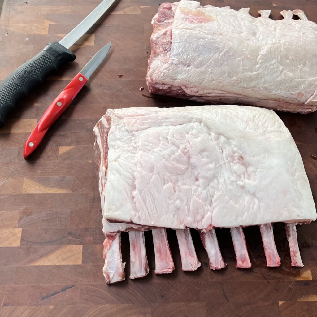 Two racks of lamb next to knives to be scored. 