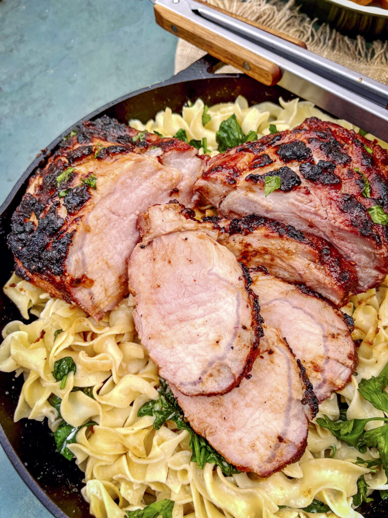 An up close photo of sliced smoked pork loin on egg noodles.