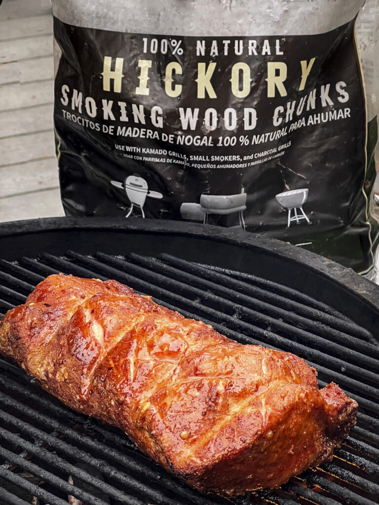 A close up shot of Hickory Smoking Wood Chunks bag and a smoked pork loin that is ready to be taken off the grill.
