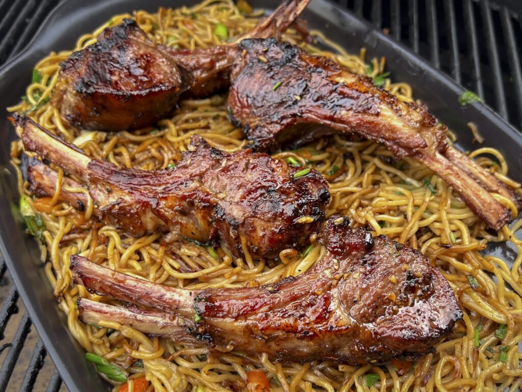Ramen is on a black platter with cooked lamb chops on top. 