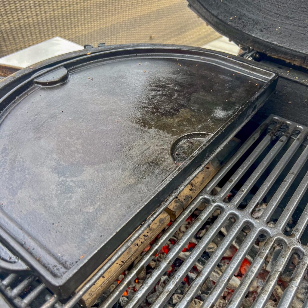 A griddle over indirect heat on a grill. On the opposite side is a grill grate over direct heat. 