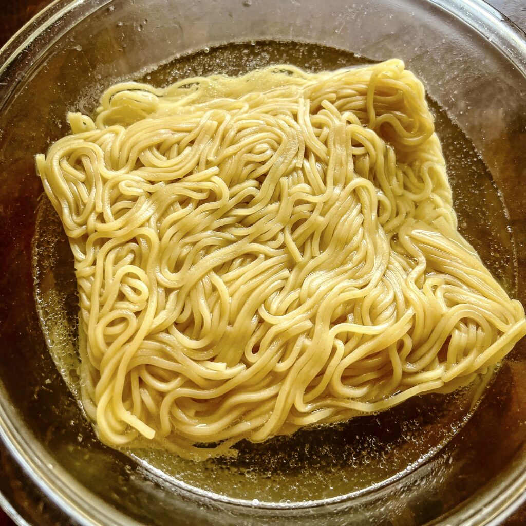 Ramen is in a bowl waiting to go on the grill. 