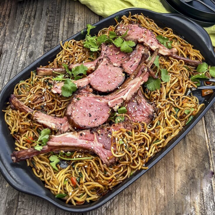 A black platter with ramen and sliced lamb chops.