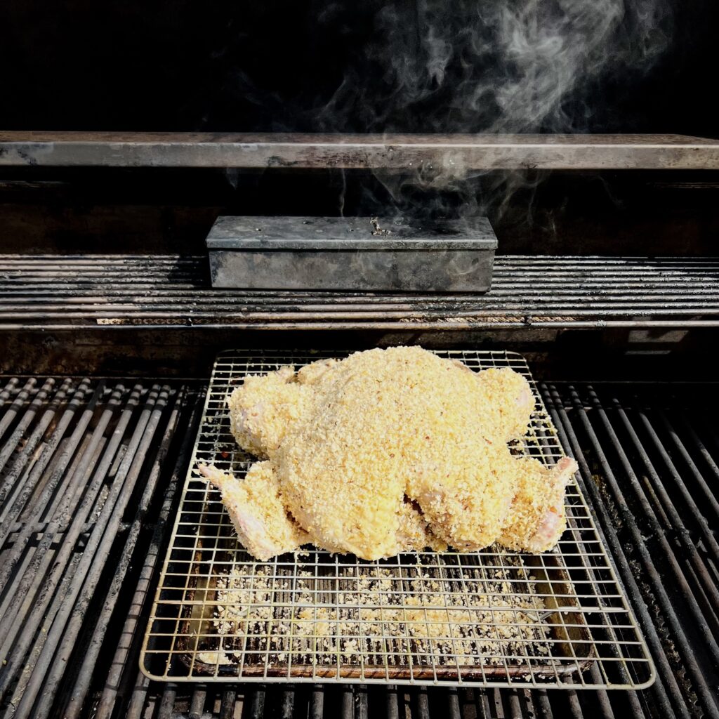 A crumb coated chicken on a gas grill is being baked.