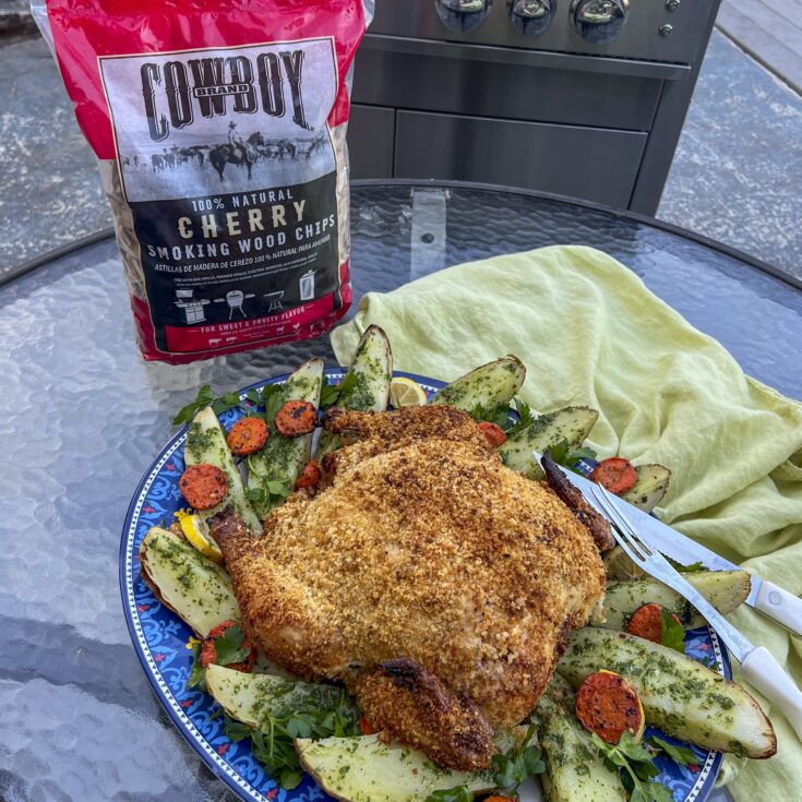 Parmesan Panko Grilled Whole Chicken is on a platter next to cherry wood chips.
