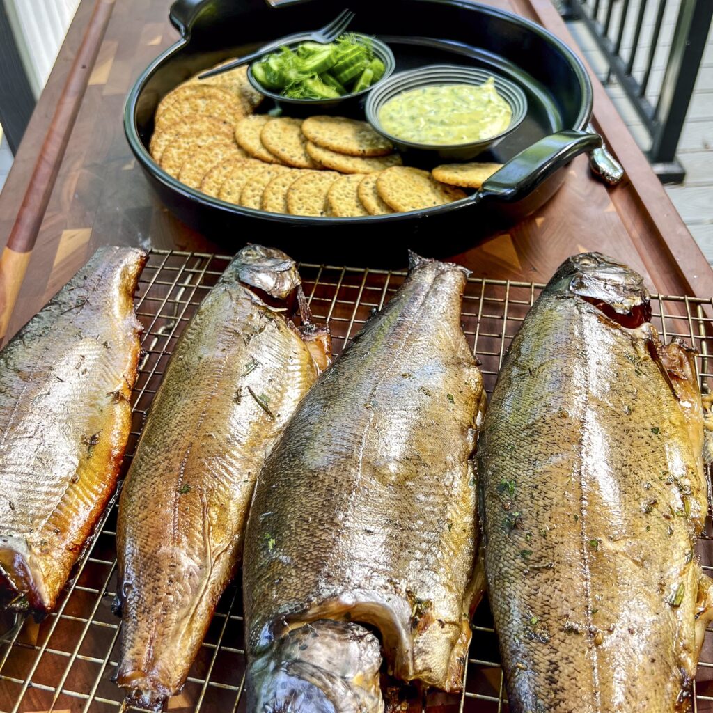 Four smoked trout are on the cutting board ready to be added to a platter of crackers and dill sauce. 